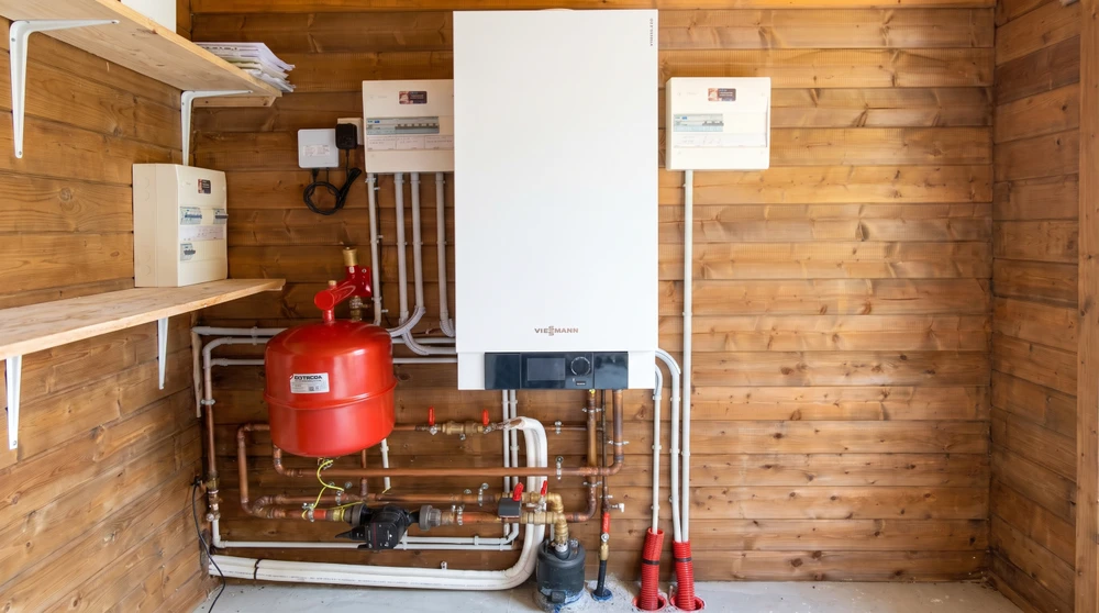 Technicien en combinaison noire et rouge, accroupi, effectue la maintenance d'une pompe à chaleur air/air (PAC) murale extérieure