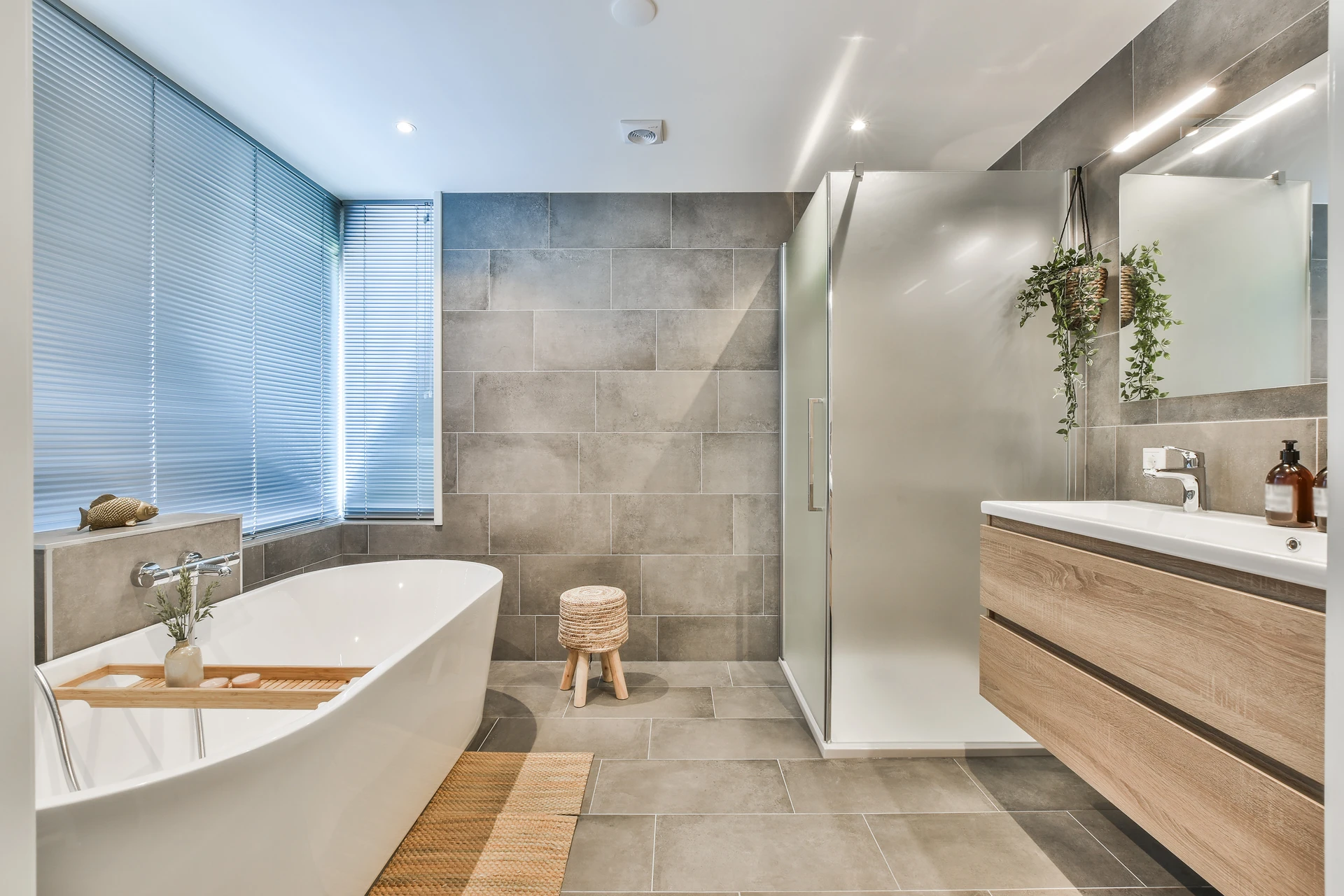 Salle de bain moderne avec douche italienne, baignoire blanche, meuble vasque double en bois clair suspendu, miroir rétroéclairé et sèche-serviettes mural