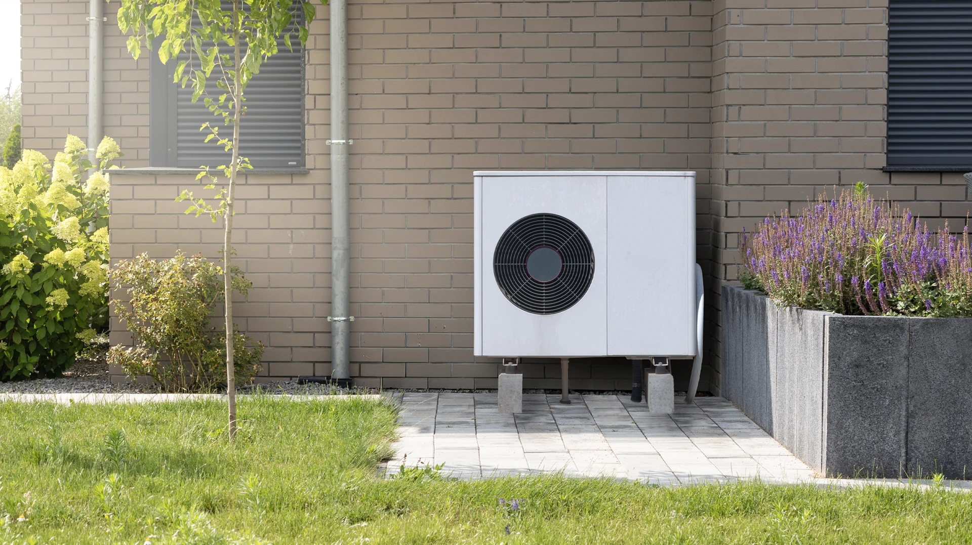 Extérieur résidentiel moderne avec pompe à chaleur air-eau installée sur socle béton devant maison contemporaine