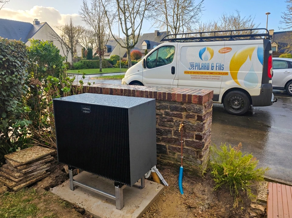 Pompe à chaleur air/eau monobloc noire installée en extérieur, fixée sur socle béton avec châssis inox